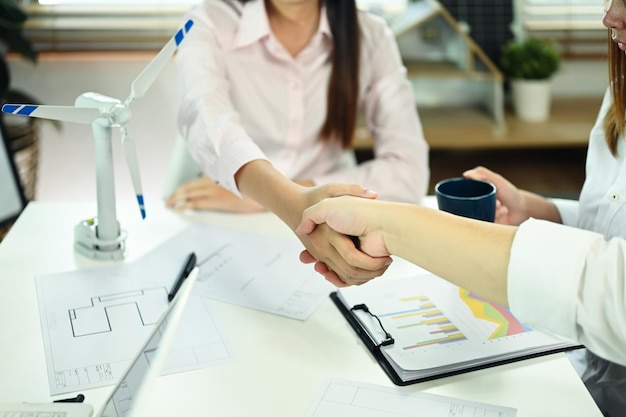 Mujer de negocios e ingeniero estrechando la mano en una mesa de reuniones Concepto de desarrollo de energía verde