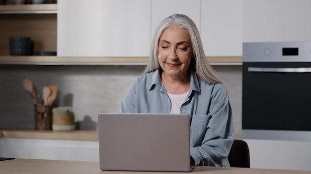 Mujer de negocios de edad avanzada caucásica, independiente, abuelita, compradora, compradora, trabaja en una computadora portátil desde casa
