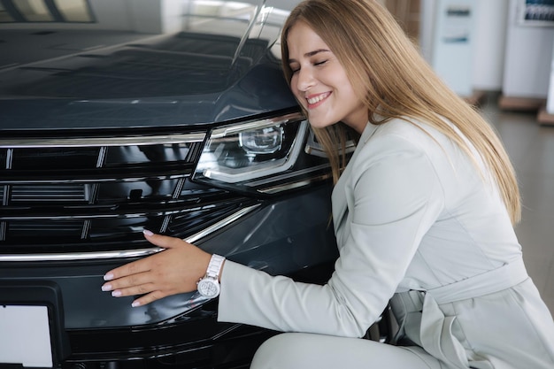 Mujer de negocios eligiendo un auto nuevo en una sala de exhibición de autos feliz abrazo femenino auto nuevo y muy contento elegante