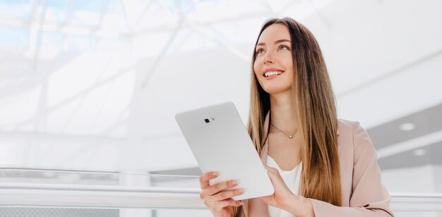 Mujer de negocios se encuentra en el interior de un edificio de oficinas sosteniendo una tableta y sonriendo