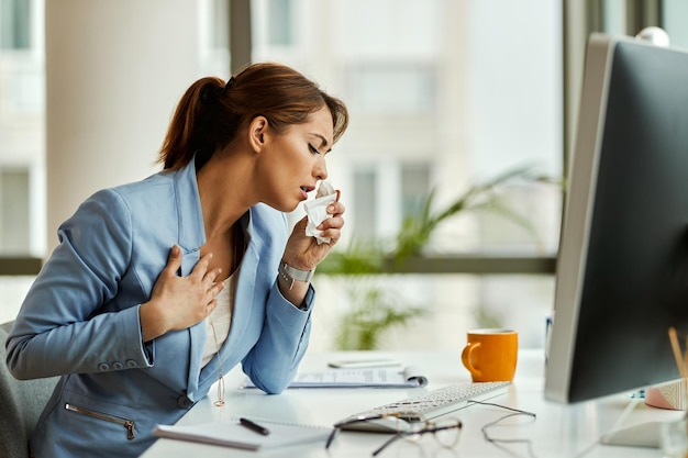 Mujer de negocios enferma y tosiendo mientras trabaja en una computadora en la oficina