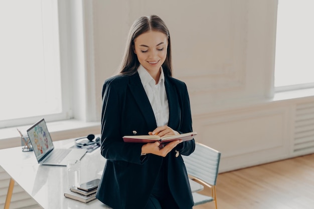 Mujer de negocios enfocada escribiendo un plan de negocios en un cuaderno mientras se apoya en el escritorio