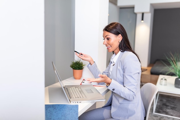 Mujer de negocios enfocada usando una computadora portátil en casa mirando la pantalla hablando leyendo o escribiendo correos electrónicos sentada en el sofá sonriendo estudiante haciendo la tarea trabajando en un proyecto de investigación en línea
