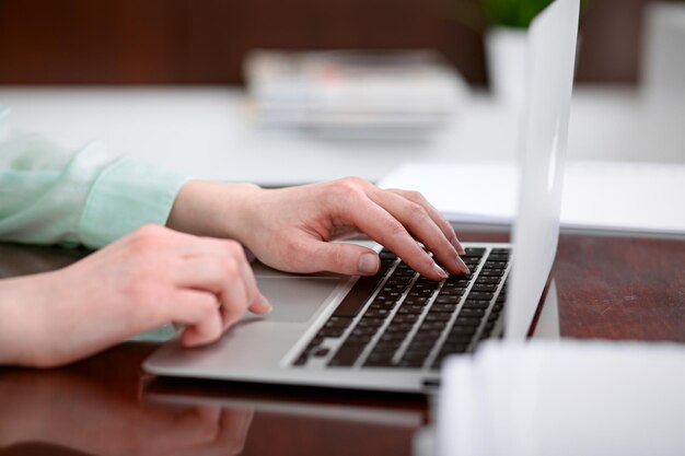 Mujer de negocios entrega una blusa verde sentada en el escritorio de la oficina y escribiendo en la computadora portátil