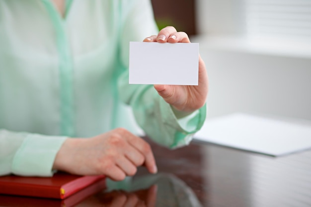 Mujer de negocios entrega una blusa verde sentada en un escritorio en una oficina y sostiene una tarjeta de presentación.