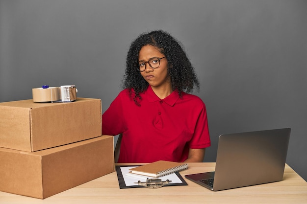 Mujer de negocios de entregas con inventario y cajas infeliz mirando a la cámara con expresión sarcástica