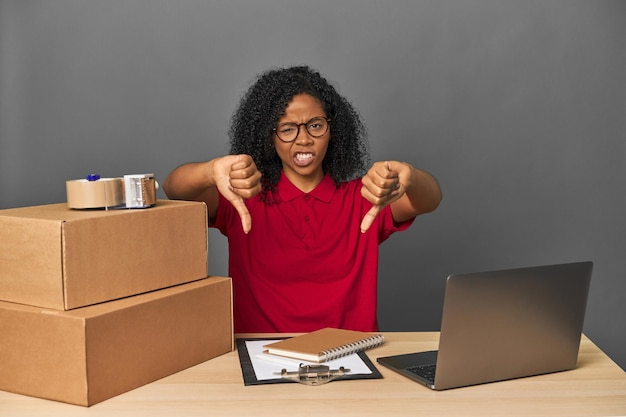 Foto mujer de negocios de entregas con inventario y cajas mostrando el pulgar hacia abajo y expresando aversión