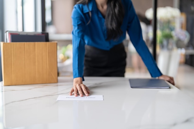 Mujer de negocios enviando una carta de renuncia y empacando cosas Renunciar Deprimir o llevar una caja de cartón de negocios junto al escritorio en la oficina Cambio de trabajo o despedida de la empresa