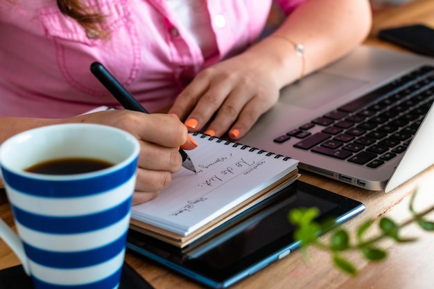 Foto mujer de negocios escribiendo en un libro mientras usa una computadora portátil en el escritorio