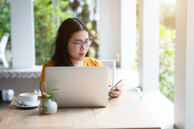 Mujer de negocios y escribir un mensaje en un teléfono inteligente que trabaja informalmente con una computadora portátil