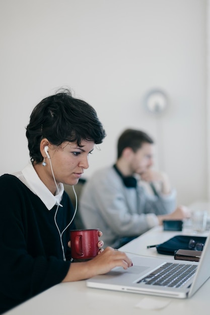 Mujer de negocios escuchando música mientras trabaja en la oficina con antecedentes de colegas masculinos