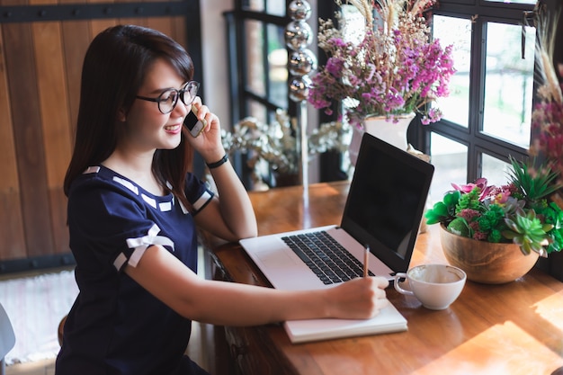 Mujer de negocios espera recoger Smartphone trabajando con la computadora portátil en la cafetería