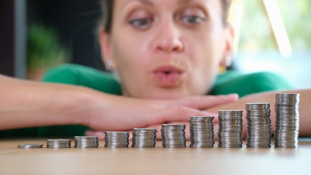 La mujer de negocios esperanzada piensa cómo aumentar las ganancias y las pilas de monedas en la mesa y