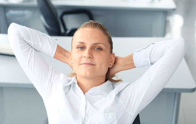 Mujer de negocios se está relajando con las manos detrás de la cabeza y sentada en una silla en la oficina