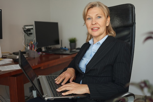 Una mujer de negocios está sentada en un escritorio de oficina con una computadora portátil.