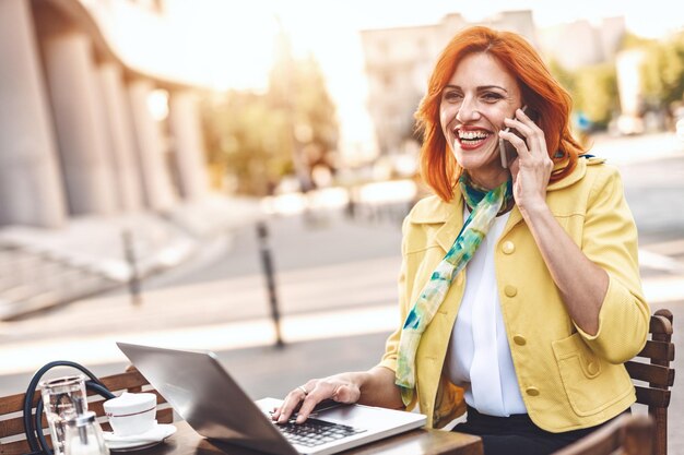 La mujer de negocios está trabajando en la computadora portátil y usando un teléfono inteligente en un descanso para tomar café en un café de la calle.