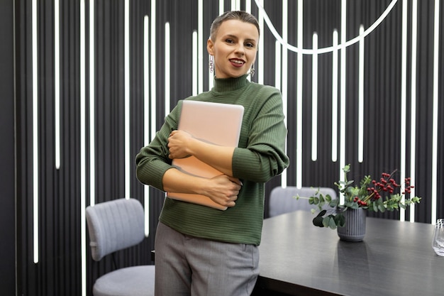 Mujer de negocios con estilo con una computadora portátil en sus manos en el fondo de una oficina moderna