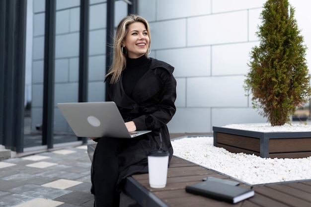 Mujer de negocios con estilo durante un descanso tomando café en la calle con una computadora portátil en las manos