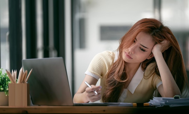 Mujer de negocios estresada molesta en el trabajo Mujer de negocios asiática hermosa joven ocupada que sufre estrés trabajando en la computadora de la oficina