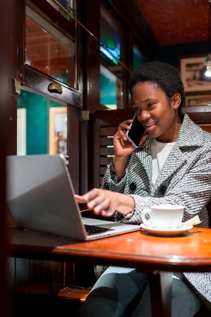 Mujer de negocios de etnia africana en un retrato de cafetería con una computadora hablando por teléfono