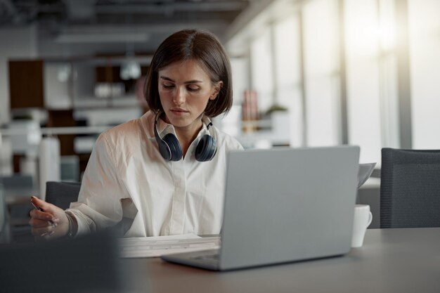 Foto mujer de negocios europea enfocada que trabaja con una computadora portátil y toma notas mientras está sentada en una oficina moderna