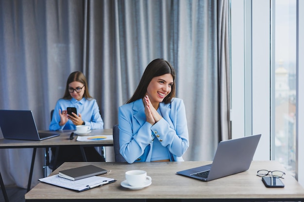 Una mujer de negocios europea está hablando por un teléfono móvil mientras su colega europeo está trabajando en segundo plano Concepto de mujeres exitosas modernas Niñas sentadas en escritorios en una oficina soleada