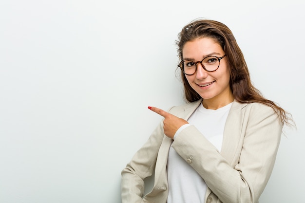 Mujer de negocios europea joven que sonríe y que señala a un lado, mostrando algo en el espacio en blanco.