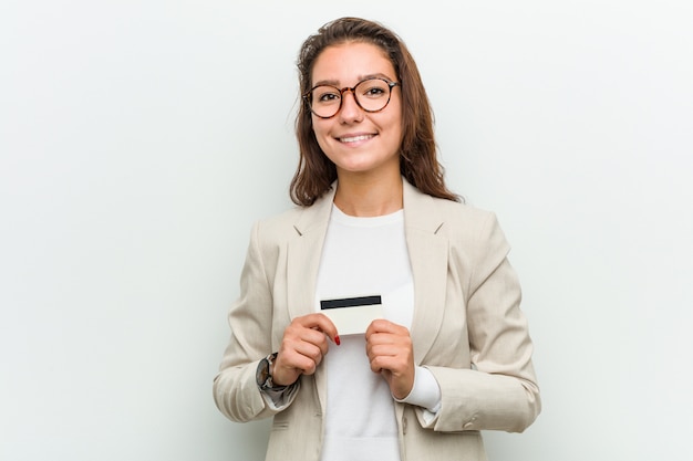 Mujer de negocios europea joven que sostiene una tarjeta de crédito feliz, sonriente y alegre.