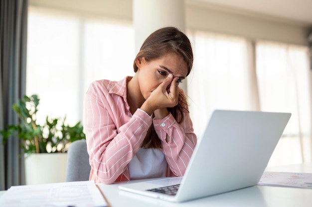 Mujer de negocios exhausta con dolor de cabeza en la oficina moderna Mujer creativa que trabaja en el escritorio de la oficina sintiéndose cansada Mujer de negocios casual estresada que siente dolor de cabeza mientras trabaja demasiado en la computadora de escritorio