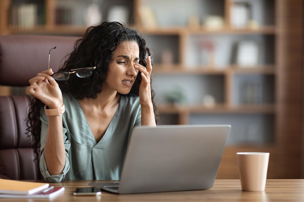 Mujer de negocios exhausta trabajando en una laptop frotándose los ojos