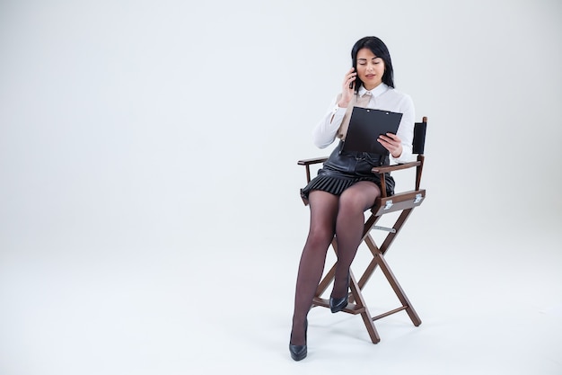 Mujer de negocios exitosa con una camisa blanca sentada en una silla con documentos y hablando sobre el negocio por teléfono.