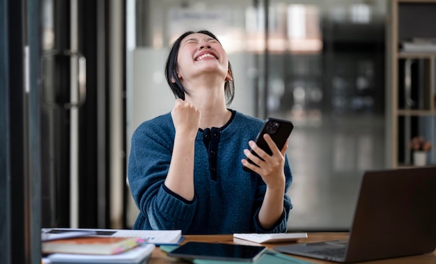 Mujer de negocios exitosa y emocionante Mujer joven emocionada de ganar en su teléfono inteligente en el trabajo