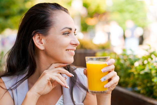 Mujer de negocios feliz en un café callejero bebe jugo natural y sonríe en un día soleado