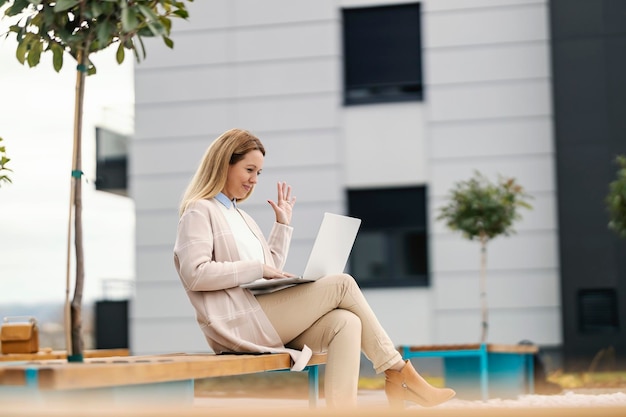 Una mujer de negocios feliz con un estilo casual inteligente está sentada en un parque en el centro y tiene una conferencia telefónica