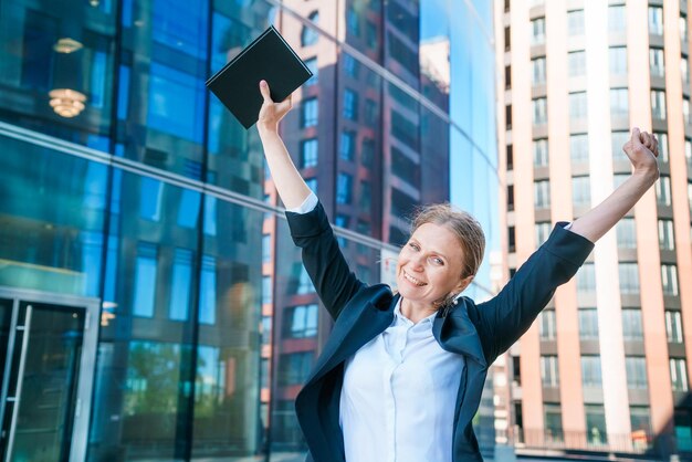Mujer de negocios feliz mostrando los pulgares hacia arriba mientras está de pie al aire libre contra la oficina