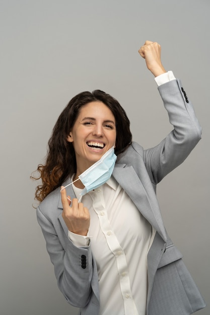 mujer de negocios feliz quitándose la máscara, levantando el puño, estudio, Covid-19 terminó. La pandemia ha terminado.