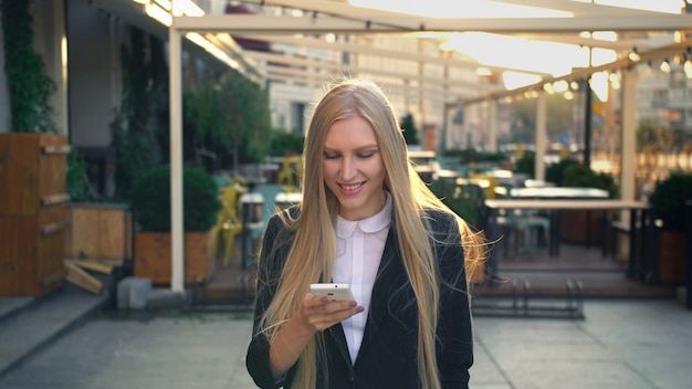 Mujer de negocios formal caminando en la calle mientras mira su teléfono