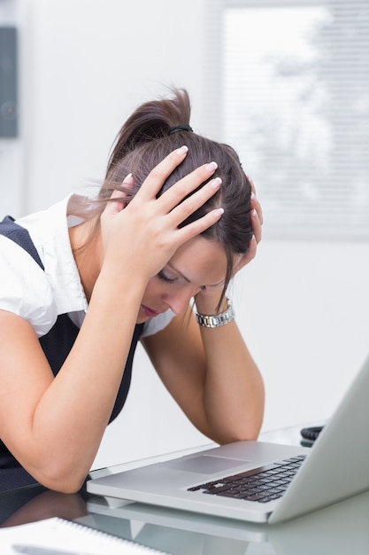 Mujer de negocios frustrados con la cabeza en las manos delante de la computadora portátil