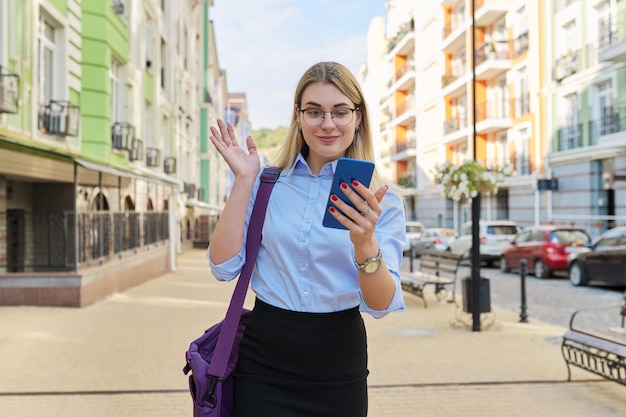 Mujer de negocios con gafas en camisa azul con bolsa para computadora portátil con teléfono inteligente