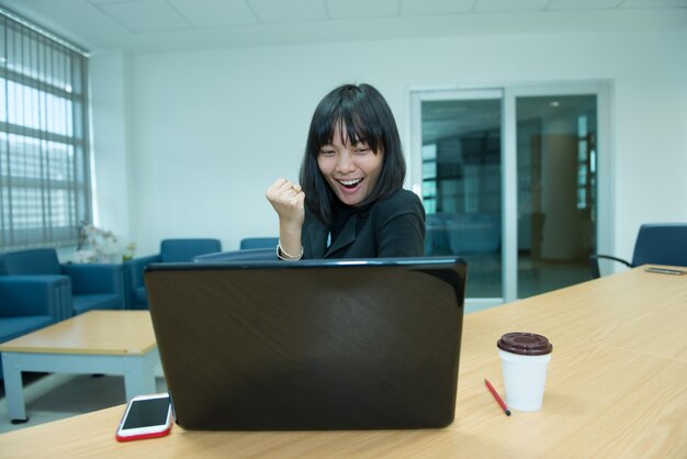 Mujer de negocios guau desde la computadora portátilMirando el mercado de valoresFeliz concepto de mujer tailandesaSecretaria trabajando en la oficina