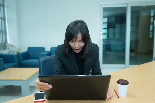 Mujer de negocios guau desde la computadora portátilMirando el mercado de valoresFeliz concepto de mujer tailandesaSecretaria trabajando en la oficina