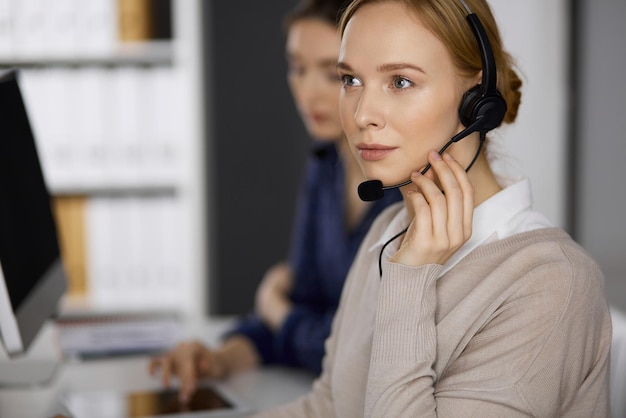 Mujer de negocios hablando por auriculares mientras está sentada en la oficina. Centro de llamadas y grupo de personas diversas en los negocios.