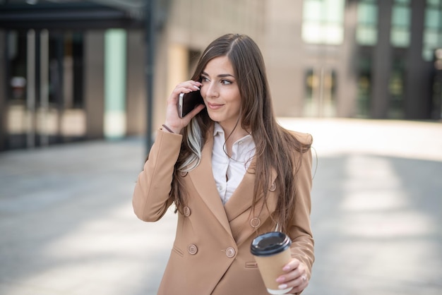 Mujer de negocios hablando por teléfono en una calle de la ciudad mientras bebe café