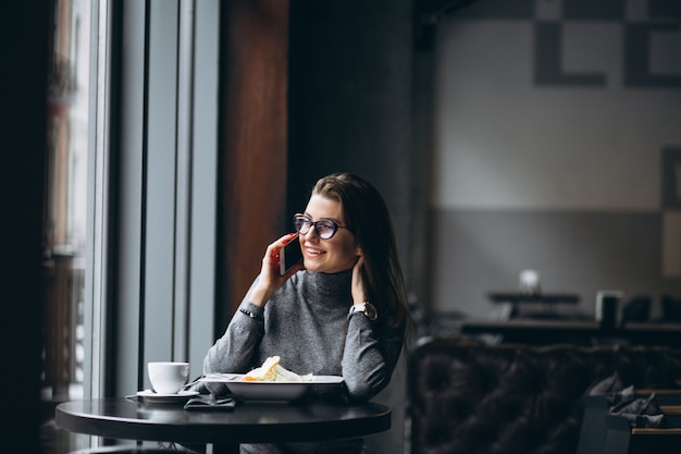 Mujer de negocios hablando por teléfono y comiendo ensalada en un café