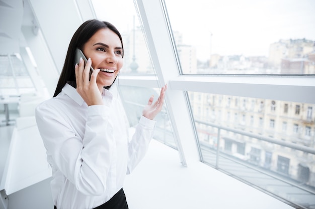 Mujer de negocios hablando por teléfono y de pie cerca de la ventana