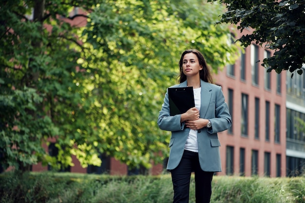 Mujer de negocios hermosa exitosa en traje con documento caminando a la reunión cerca de la oficina moderna