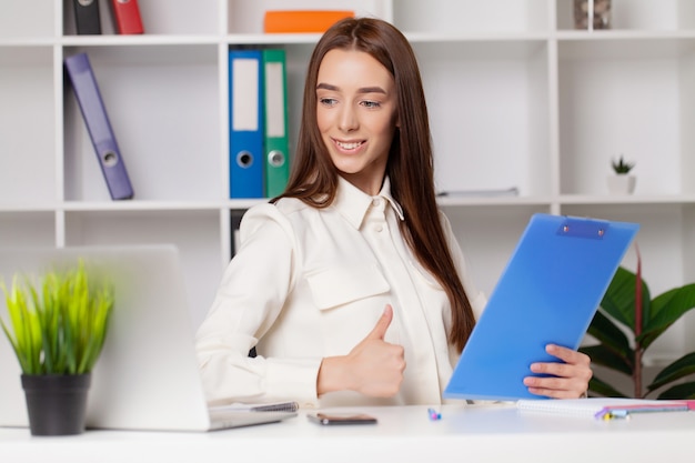 Mujer de negocios hermosa feliz con el portapapeles en la oficina.