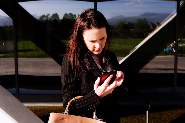 Mujer de negocios hermosa joven en la calle en la zona comercial revisando informes en el teléfono inteligente. concepto de verificación de correo en el teléfono inteligente