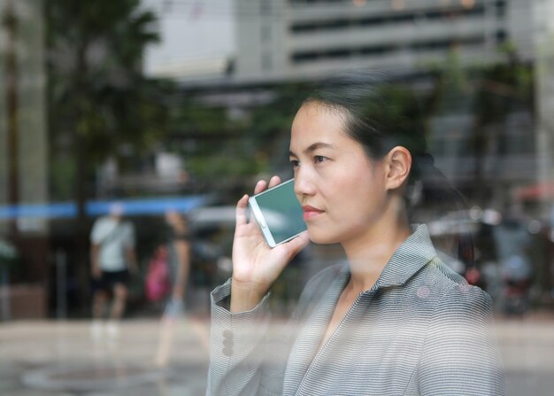 Mujer de negocios hermosa que usa un smartphone en el vidrio de reflexión del edificio de oficinas.