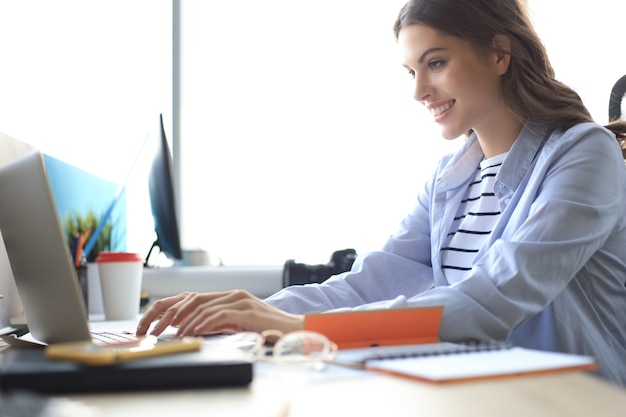 Mujer de negocios hermosa en ropa casual elegante trabajando en equipo portátil en la oficina.